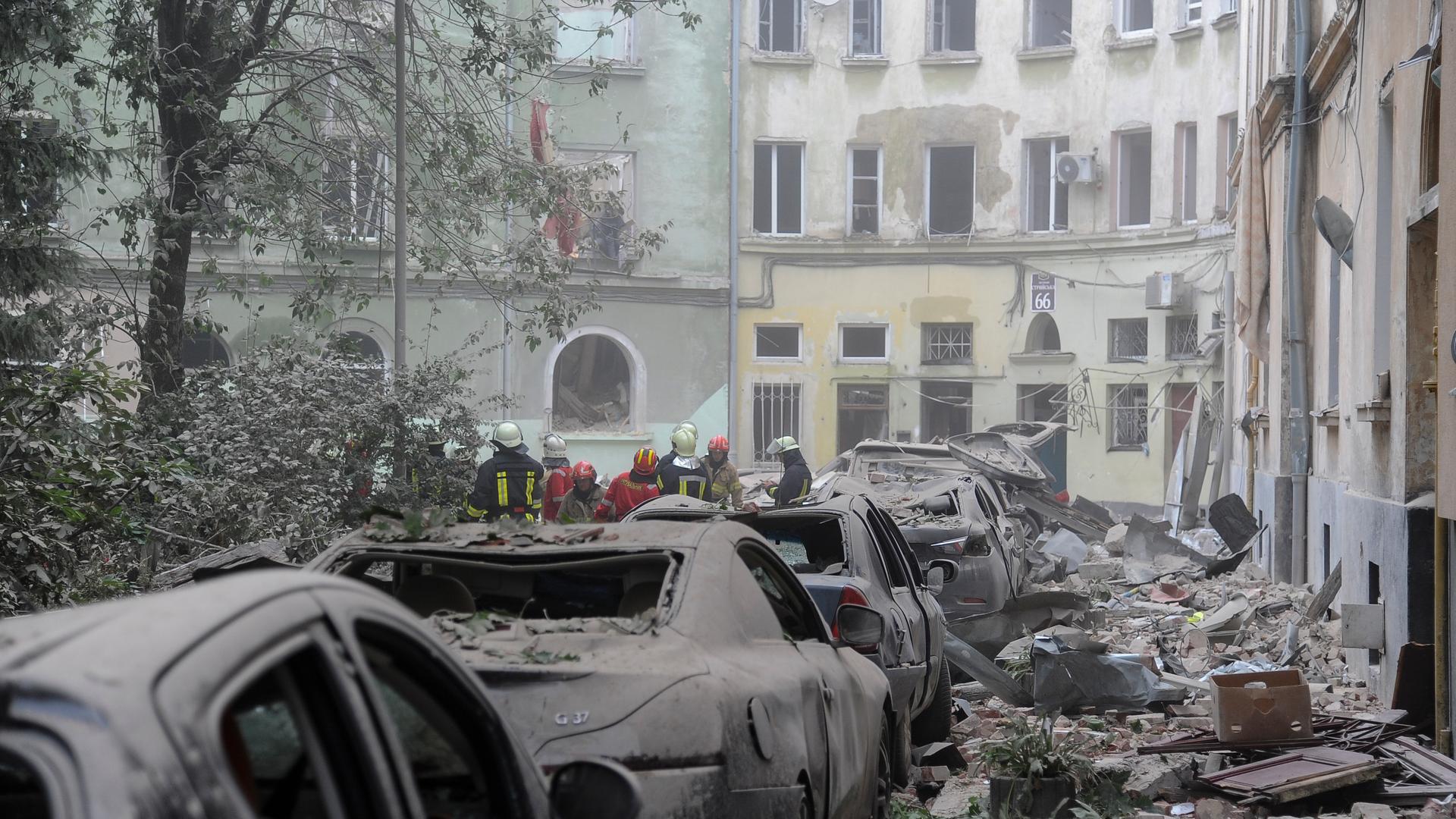 Rettungskräfte versammeln sich nach einem russischen Raketenangriff vor beschädigten Gebäuden in Lemberg. Im Vordergrund sind beschädigte Autos und Trümmer zu sehen. Rettungskräfte versammeln sich nach einem russischen Raketenangriff vor beschädigten Gebäuden in Lemberg. Im Vordergrund sind beschädigte Autos und Trümmer zu sehen.