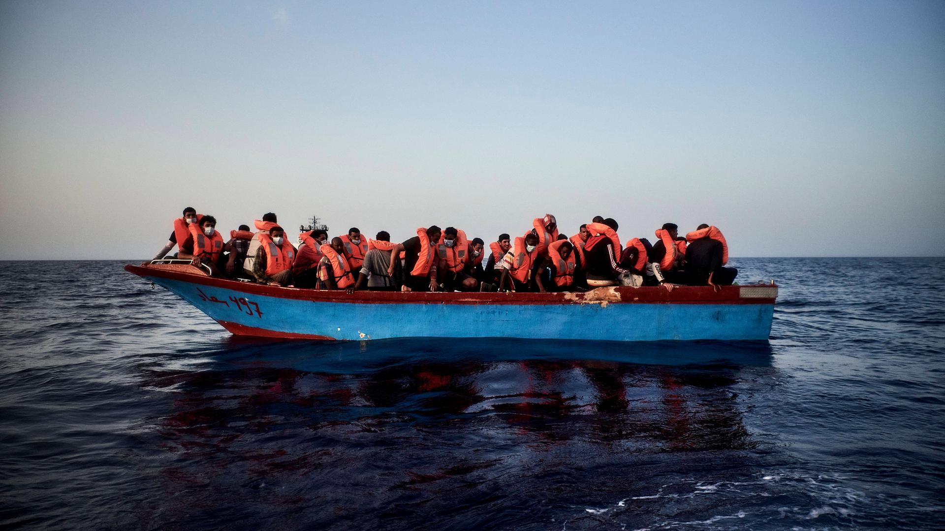Flüchtlinge mit Schwimmwesten auf einem überfüllten Boot im Meer. Flüchtlinge mit Schwimmwesten auf einem überfüllten Boot im Meer.