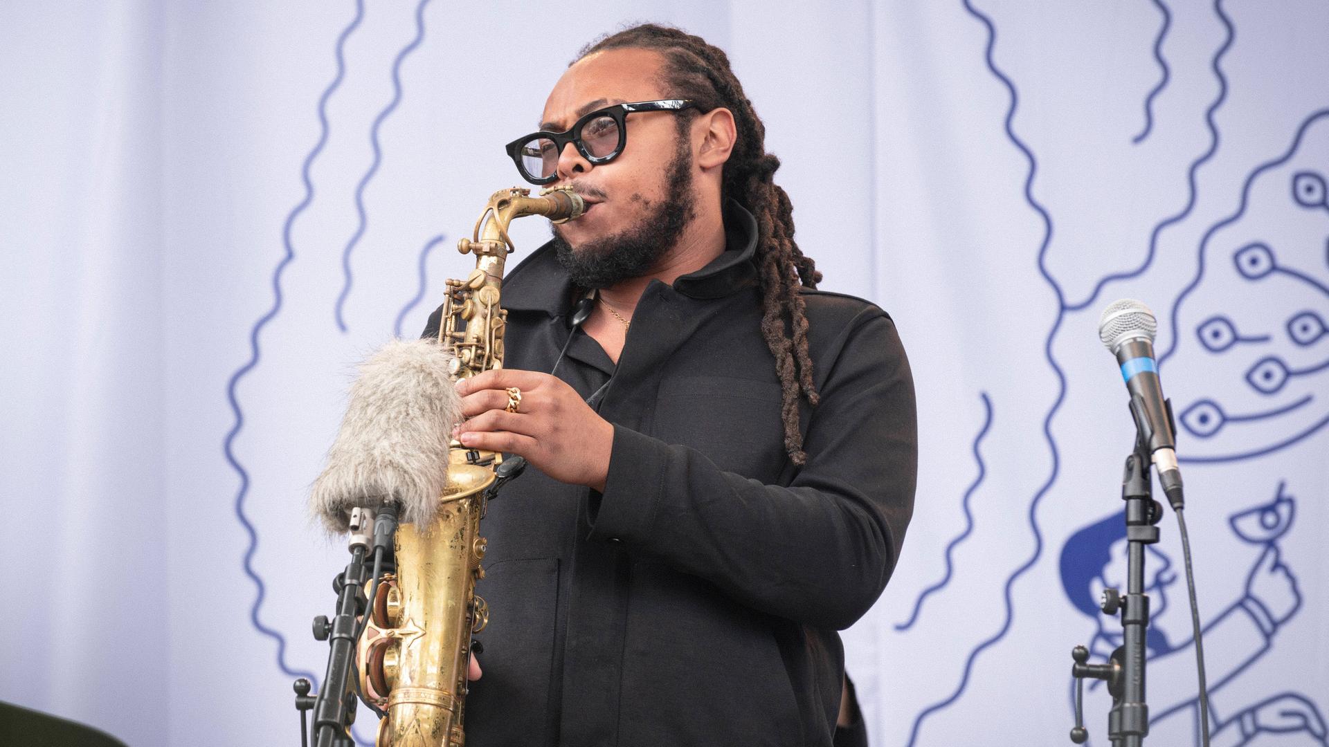 Ein Musiker mit Hornbrille und Dreadlocks spielt Saxophon. Ein Musiker mit Hornbrille und Dreadlocks spielt Saxophon.