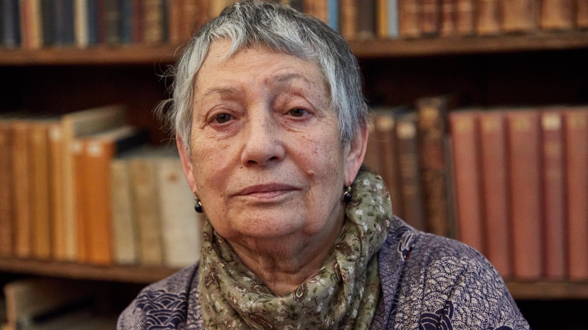 Ljudmila Ulitzkaja sitzt vor einer Bücherwand und blickt ernst in die Kamera. Ljudmila Ulitzkaja sitzt vor einer Bücherwand und blickt ernst in die Kamera.