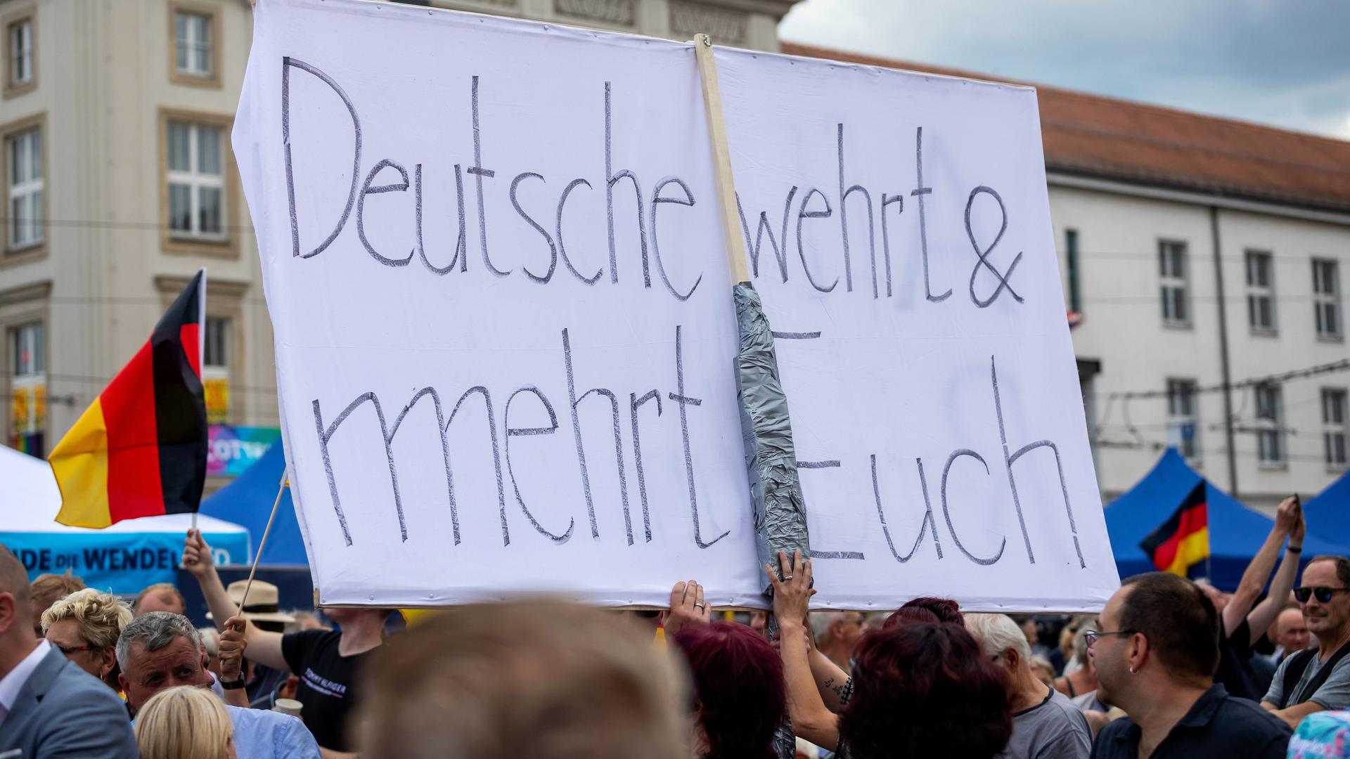 Ein Besucher einer AfD-Wahlkampfveranstaltung hält ein Transparent mit der Aufschrift "Die Deutschen verteidigen dich und mehr" hoch. Ein Besucher einer AfD-Wahlkampfveranstaltung hält ein Transparent mit der Aufschrift "Die Deutschen verteidigen dich und mehr" hoch.