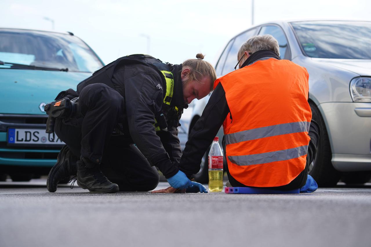 Ein Polizist versucht die Hand eines Klimaaktivisten vom Straßenbelag zu entfernen, der Aktivist Gruppe „Letzte Generation“ hat sich an auf diesen geklebt Ein Polizist versucht die Hand eines Klimaaktivisten vom Straßenbelag zu entfernen, der Aktivist Gruppe „Letzte Generation“ hat sich an auf diesen geklebt