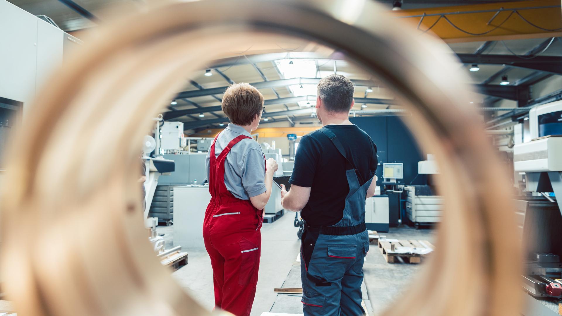 Ywei-Menschen stehen mit dem Rücken zur Kamera in einer Metallverarbeitungsanlage. Ywei-Menschen stehen mit dem Rücken zur Kamera in einer Metallverarbeitungsanlage.