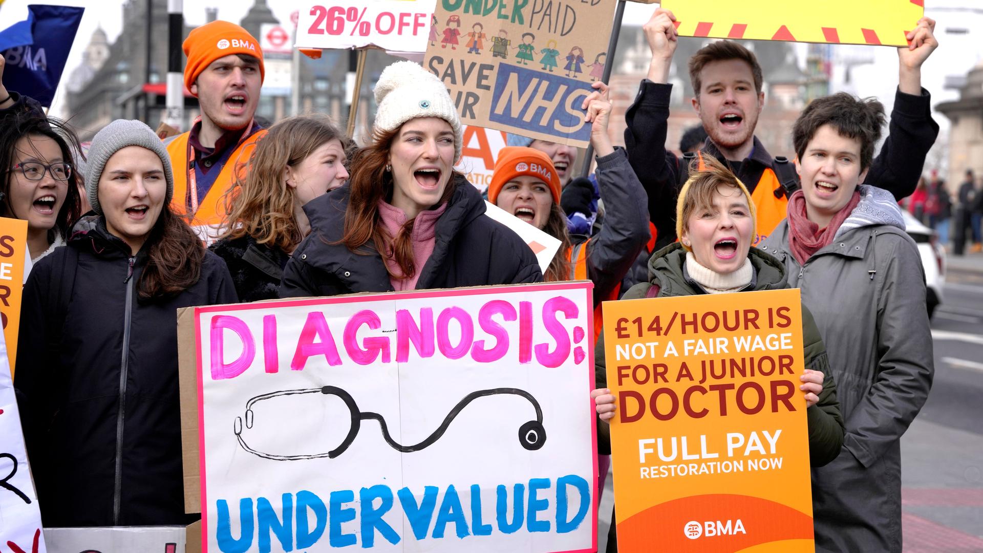 Sehen Sie streikende Männer und Frauen in Großbritannien. Sie halten Banner und Plakate hoch. steht auf einem "Diagnose unterbewertet". Sehen Sie streikende Männer und Frauen in Großbritannien. Sie halten Banner und Plakate hoch. steht auf einem "Diagnose unterbewertet".