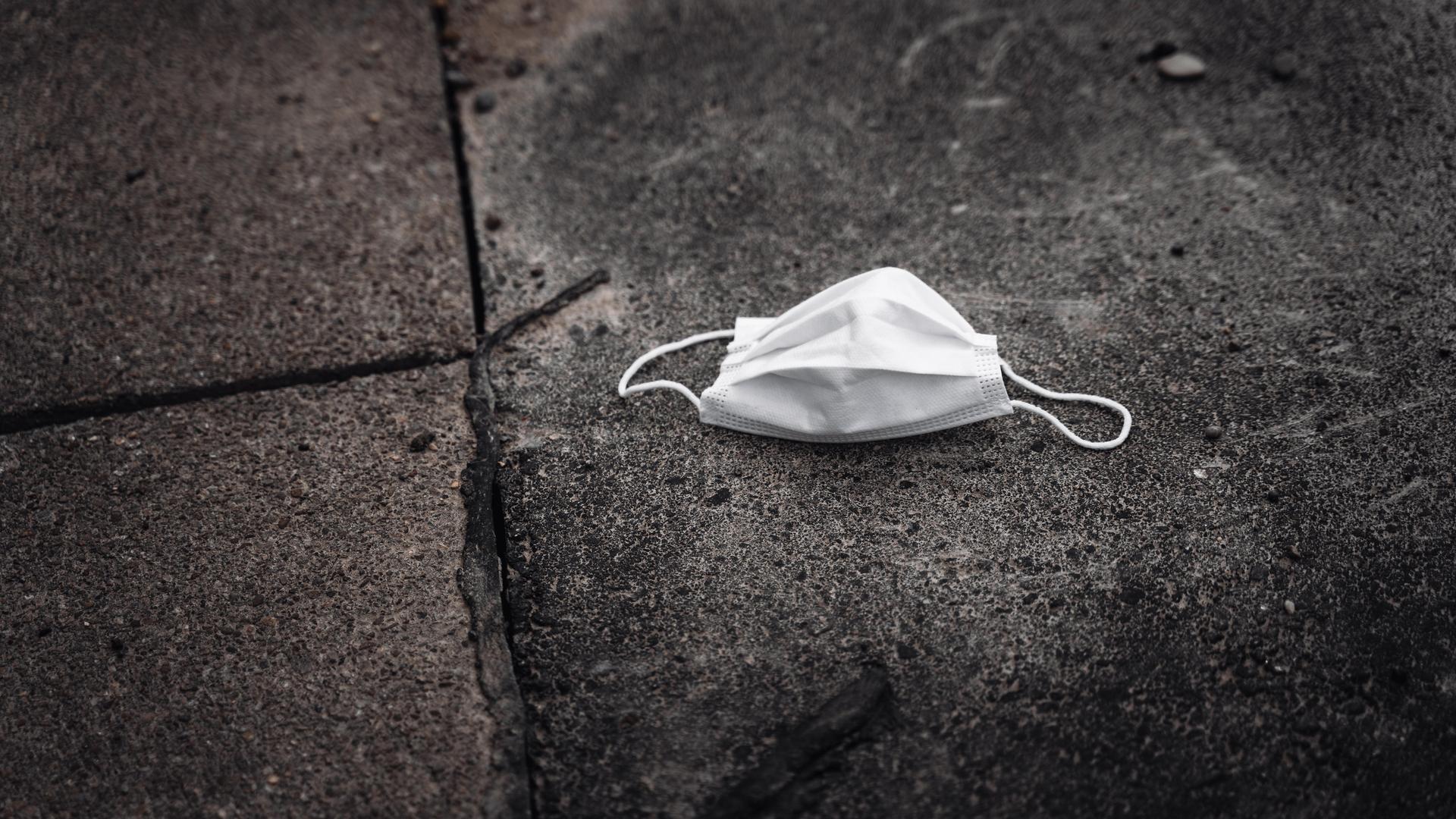 Auf dem schmutzigen Boden liegt eine weiße gebrauchte medizinische Maske. Auf dem schmutzigen Boden liegt eine weiße gebrauchte medizinische Maske.