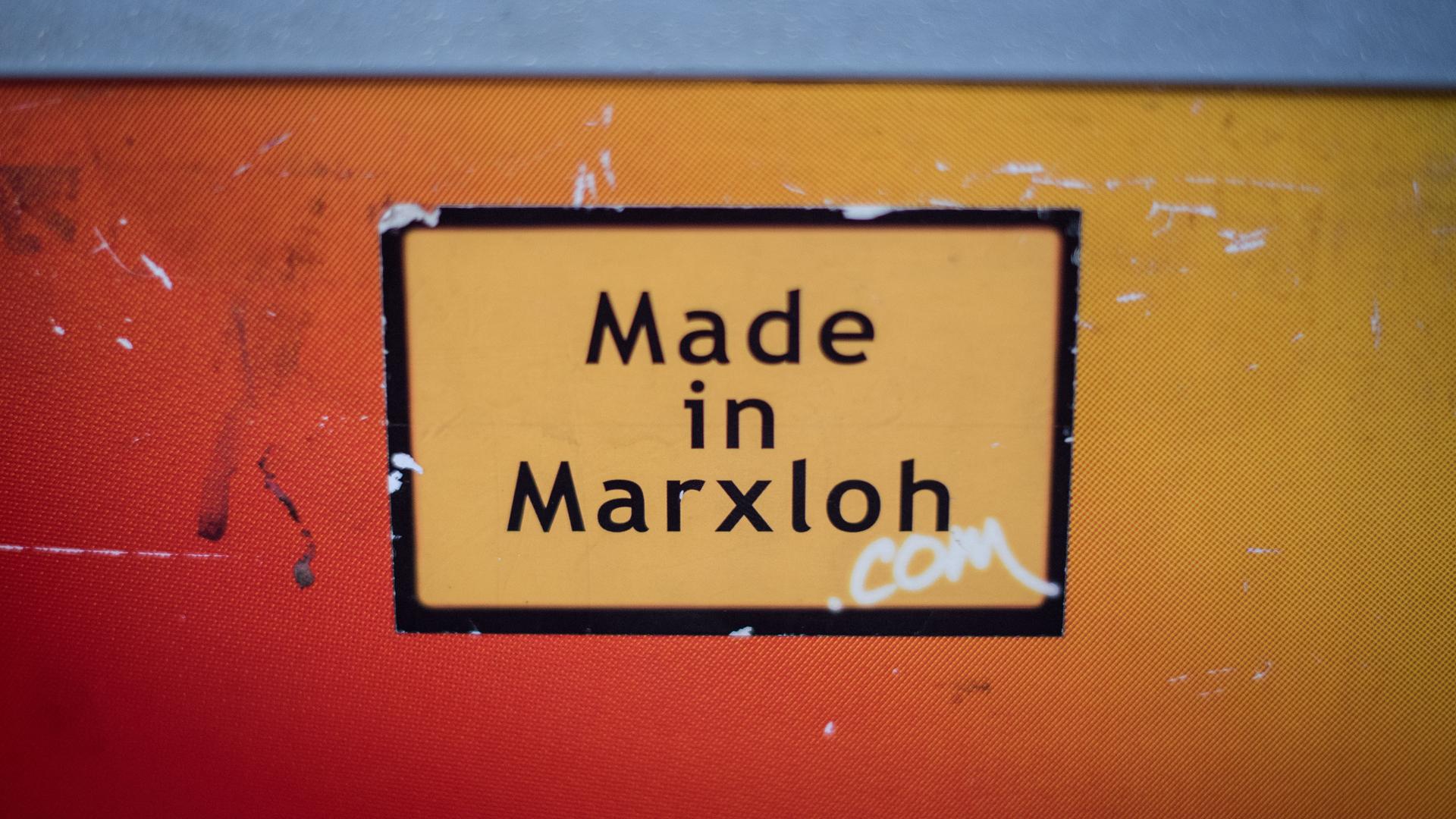 Ein Aufkleber "Hergestellt in Marxloh" klebte an einer orangefarbenen Wand. Ein Aufkleber "Hergestellt in Marxloh" klebte an einer orangefarbenen Wand.