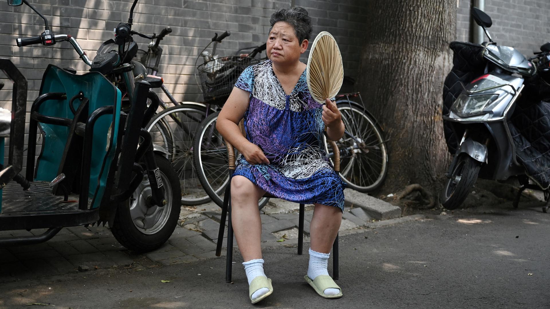 Eine Chinesin sitzt auf einem Stuhl, hält einen Fächer und sieht erschöpft aus. Eine Chinesin sitzt auf einem Stuhl, hält einen Fächer und sieht erschöpft aus.