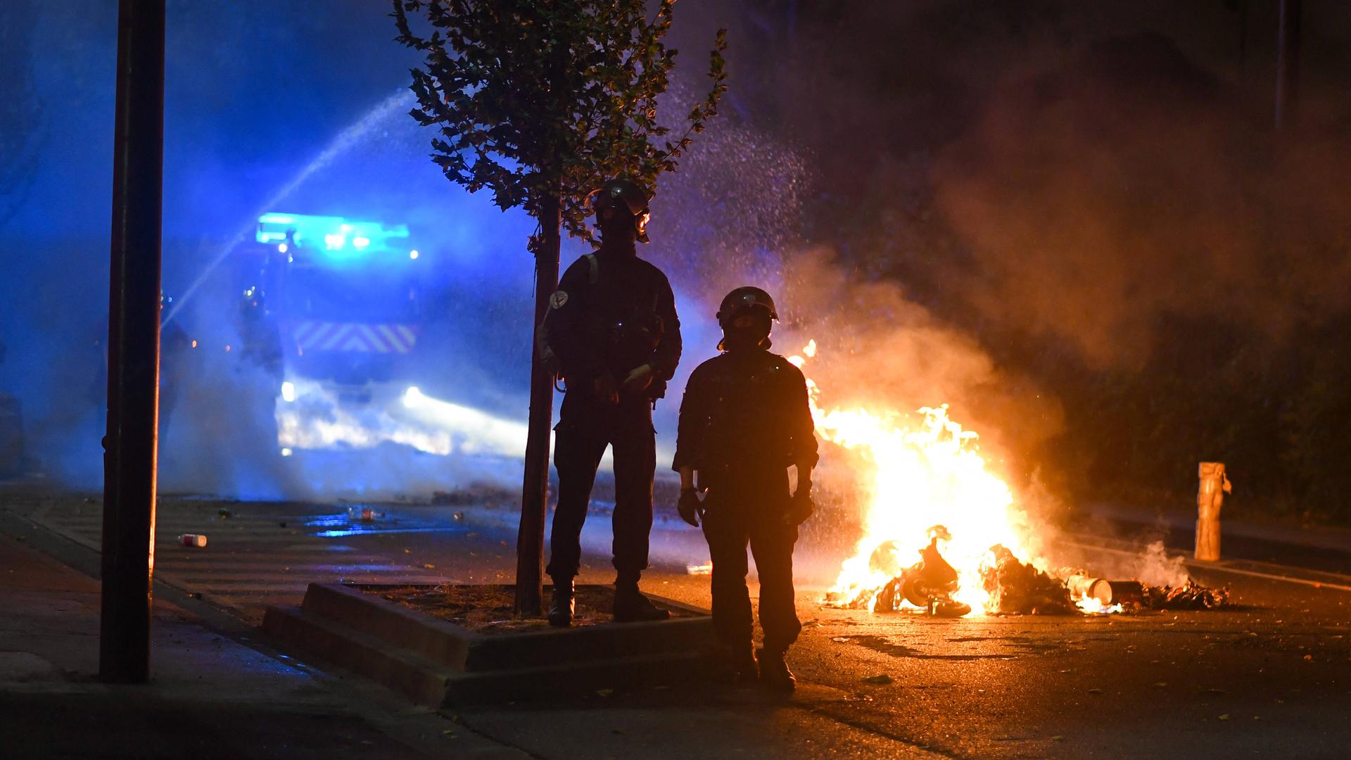 Zwei Feuerwehrleute stehen mit ihrem Einsatzfahrzeug vor einem Brand. Zwei Feuerwehrleute stehen mit ihrem Einsatzfahrzeug vor einem Brand.
