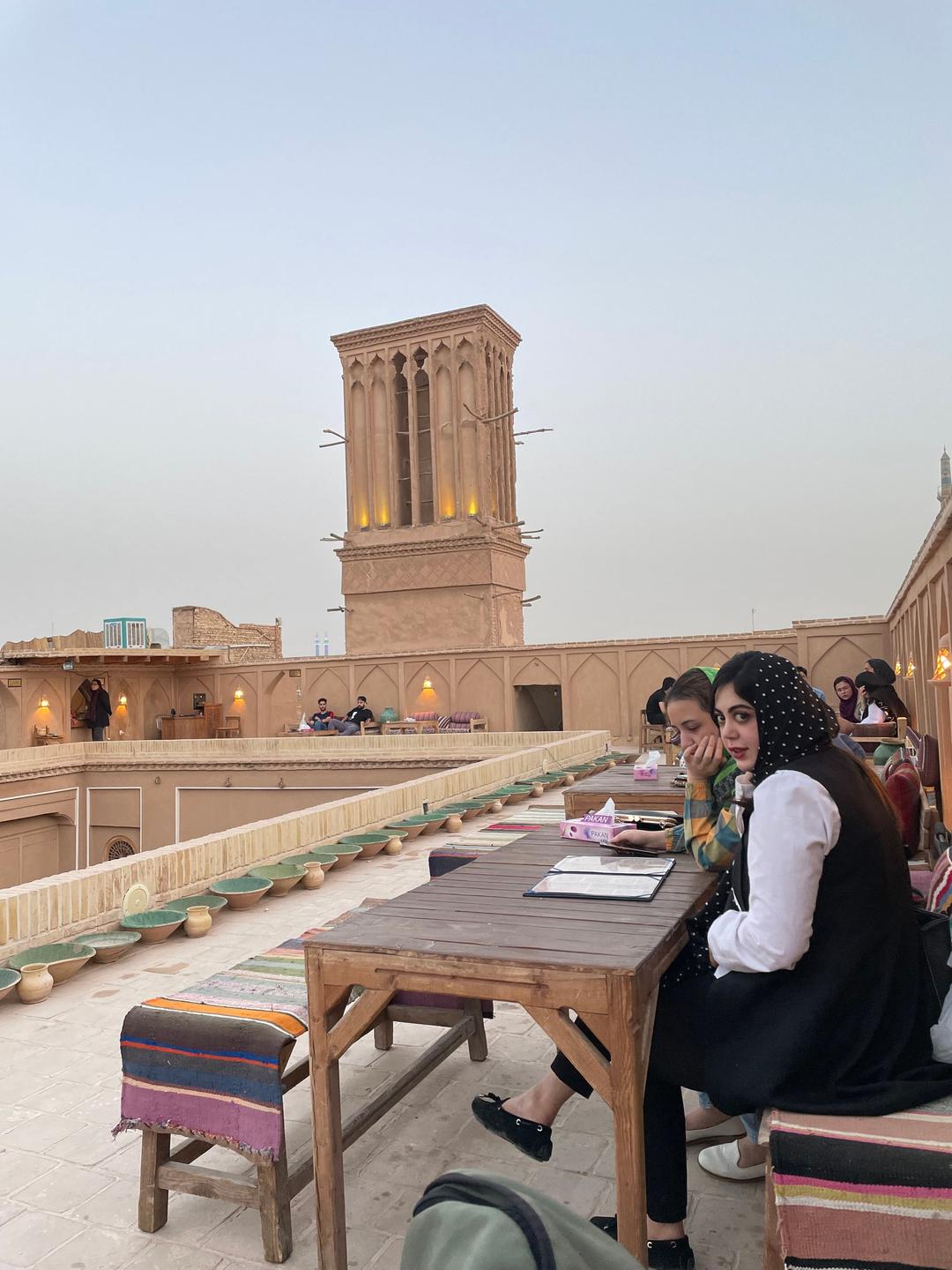 Junge Frauen sitzen an einem Tisch in einem Café auf einer Dachterrasse. Im Hintergrund ein Windturm. Junge Frauen sitzen an einem Tisch in einem Café auf einer Dachterrasse. Im Hintergrund ein Windturm.