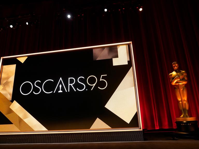 Die Bühne der 95. Oscar-Verleihungen. Vor einem Roten Samtvorhang steht eine große goldene Oscar-Figur. Daneben eine Leinwand.