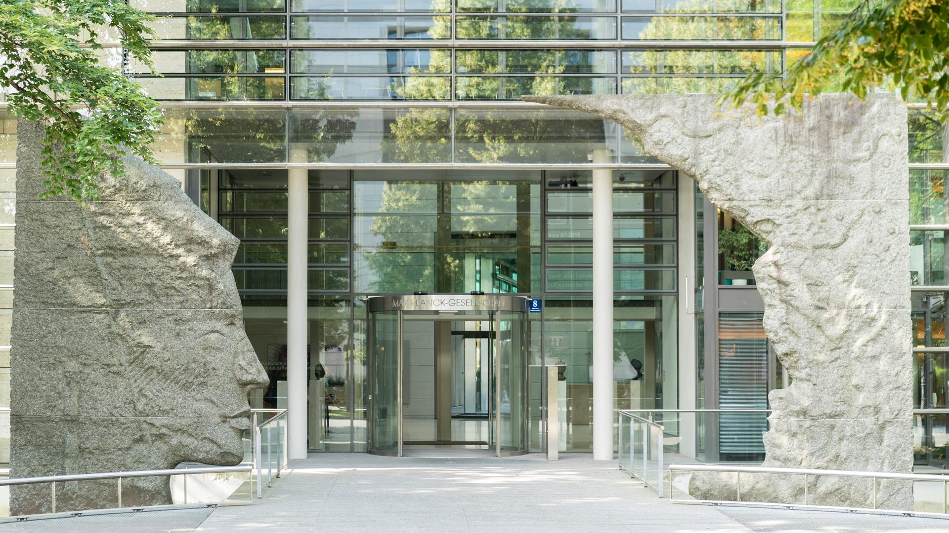 Blick auf den Eingang der Max-Planck-Gesellschaft in München, einem Glasgebäude welches am Eingang von zwei Skulpturen umrahmt wird