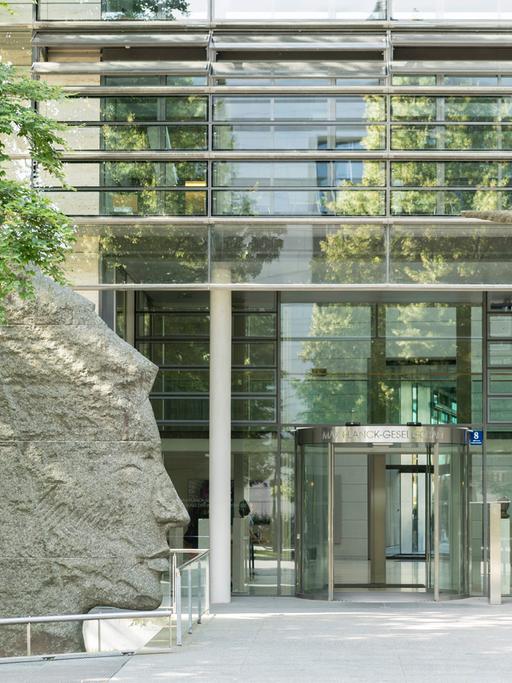 Blick auf den Eingang der Max-Planck-Gesellschaft in München, einem Glasgebäude welches am Eingang von zwei Skulpturen umrahmt wird
