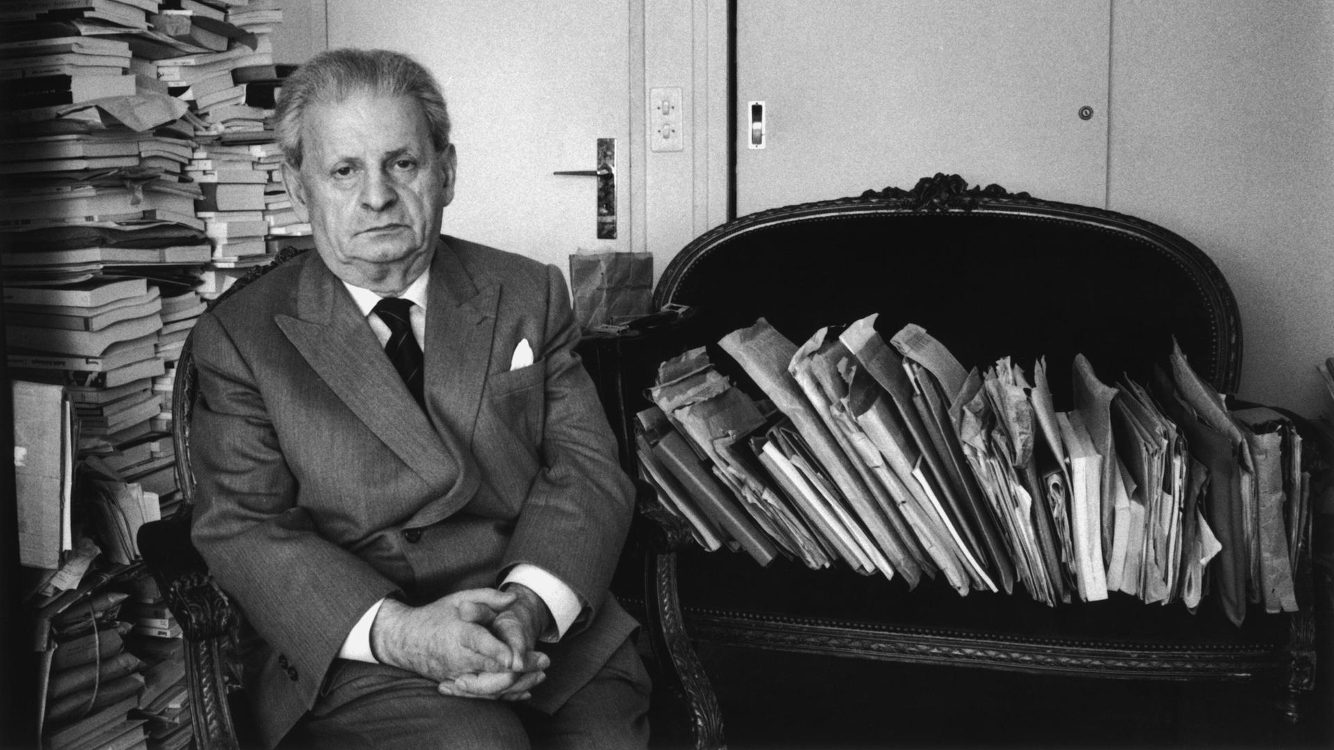 Schwarz-weiß-Porträt von Emmanuel Levinas im litauischen Kaunas. Der französische Philosoph sitzt auf einem Sessel, um ihn herum viele gestapelte Bücher, Umschläge und Zeitungen. Schwarz-weiß-Porträt von Emmanuel Levinas im litauischen Kaunas. Der französische Philosoph sitzt auf einem Sessel, um ihn herum viele gestapelte Bücher, Umschläge und Zeitungen.