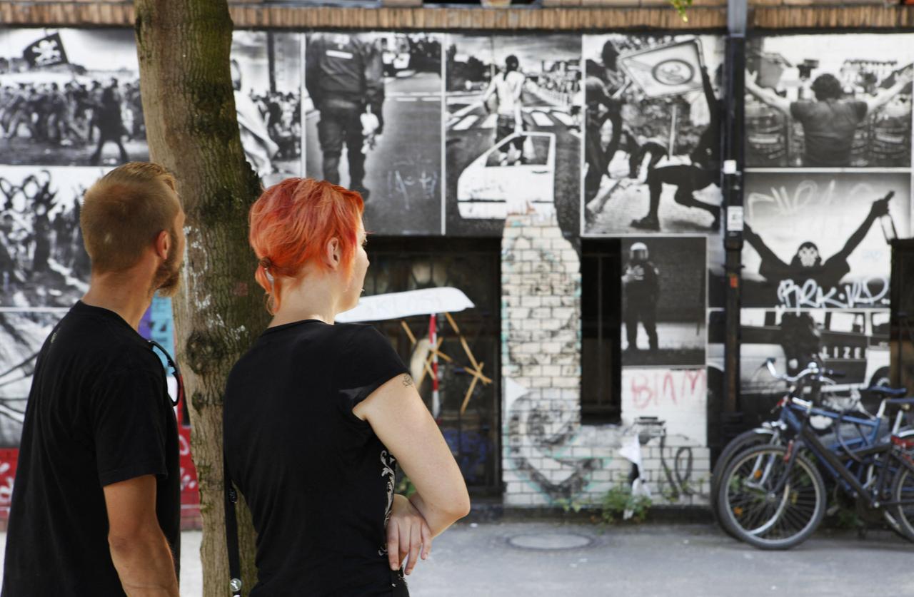 Zwei Menchen schauen auf grosse historische schwarzweiss Plakate von Haubesetzern am "Rauch-Haus" in Berlin Kreuzberg.