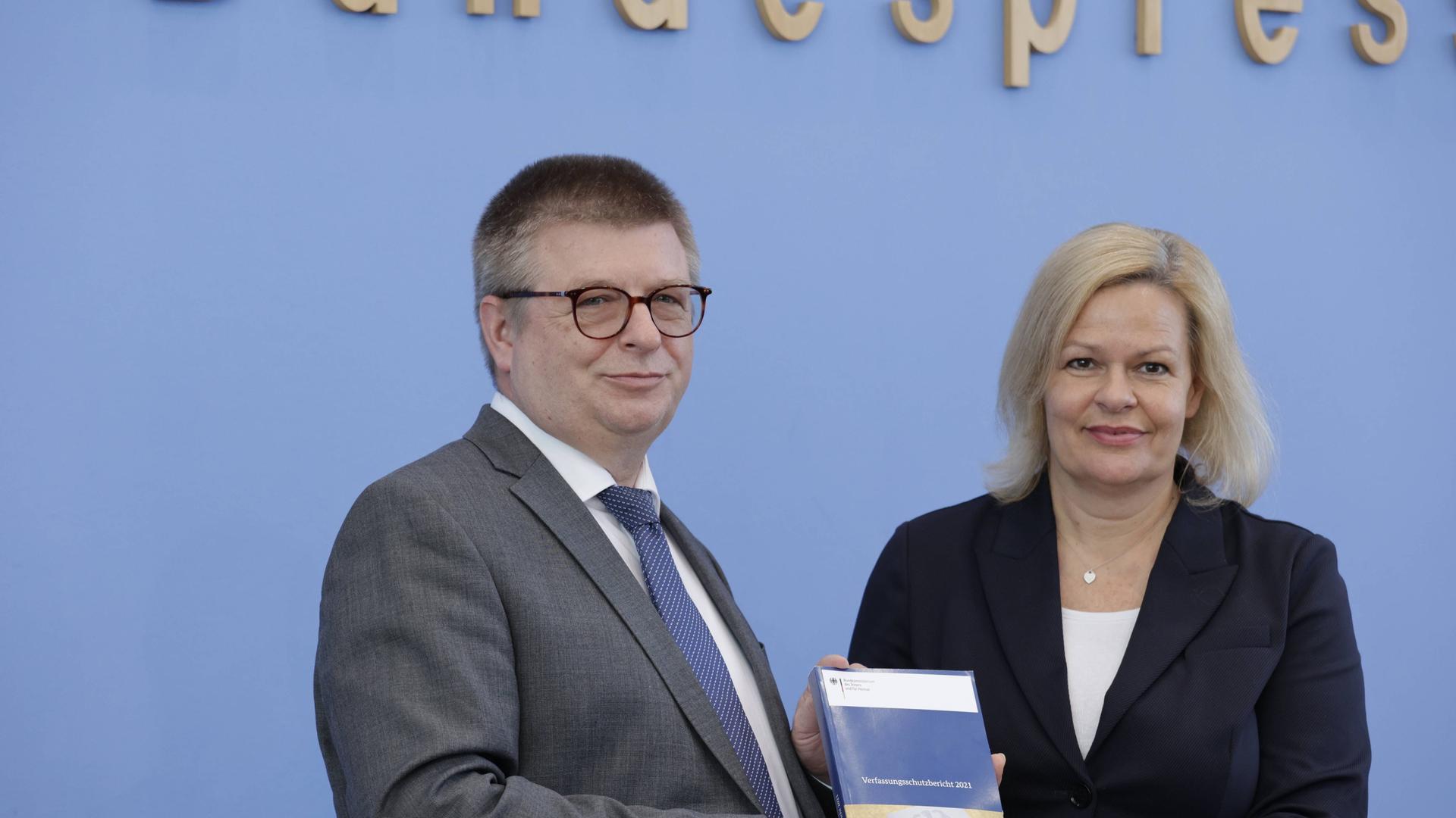 Die beiden stehen nebeneinander vor der blauen Wand der Bundespressekonferenz; Haldenwang hält den Bericht in der Hand.