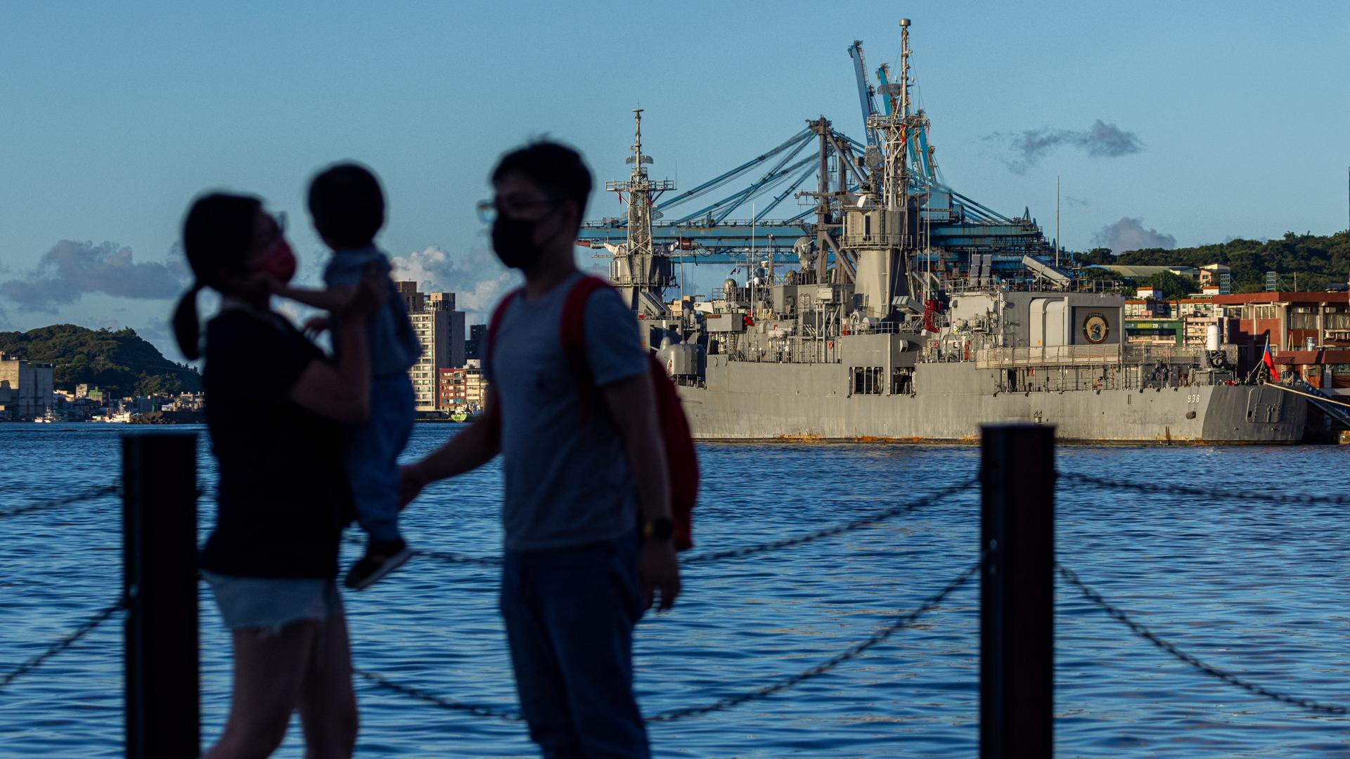 Die Silhouette einer Familie mit Kleinkind hebt sich vor einem Blick über den Hafen von Keelung ab, in dem taiwanische Militärschiffe ankern.