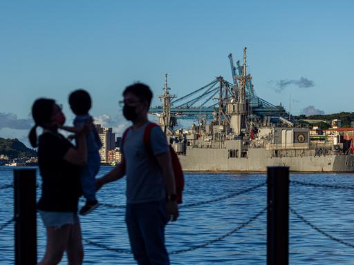 Die Silhouette einer Familie mit Kleinkind hebt sich vor einem Blick über den Hafen von Keelung ab, in dem taiwanische Militärschiffe ankern.