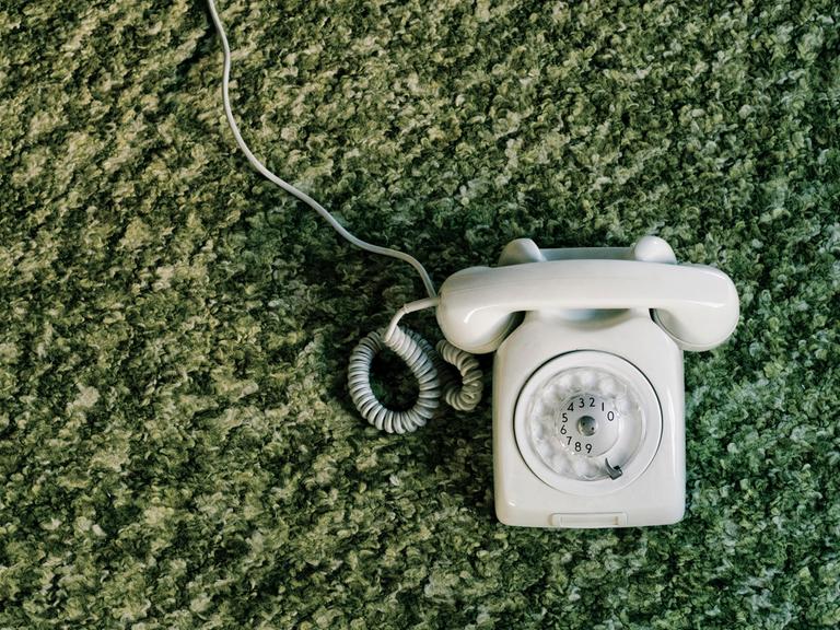 Altes Telefon mit Wählscheibe auf einem flauschigen grünenTeppich.