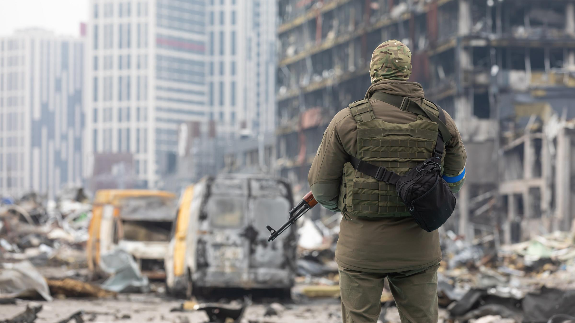 Ein ukrainischer Soldat steht mit einem Waffe in der Hand vor einem
zerstörten Gebäude in Kiew. Er dreht dem Betrachter den Rücken
zu.