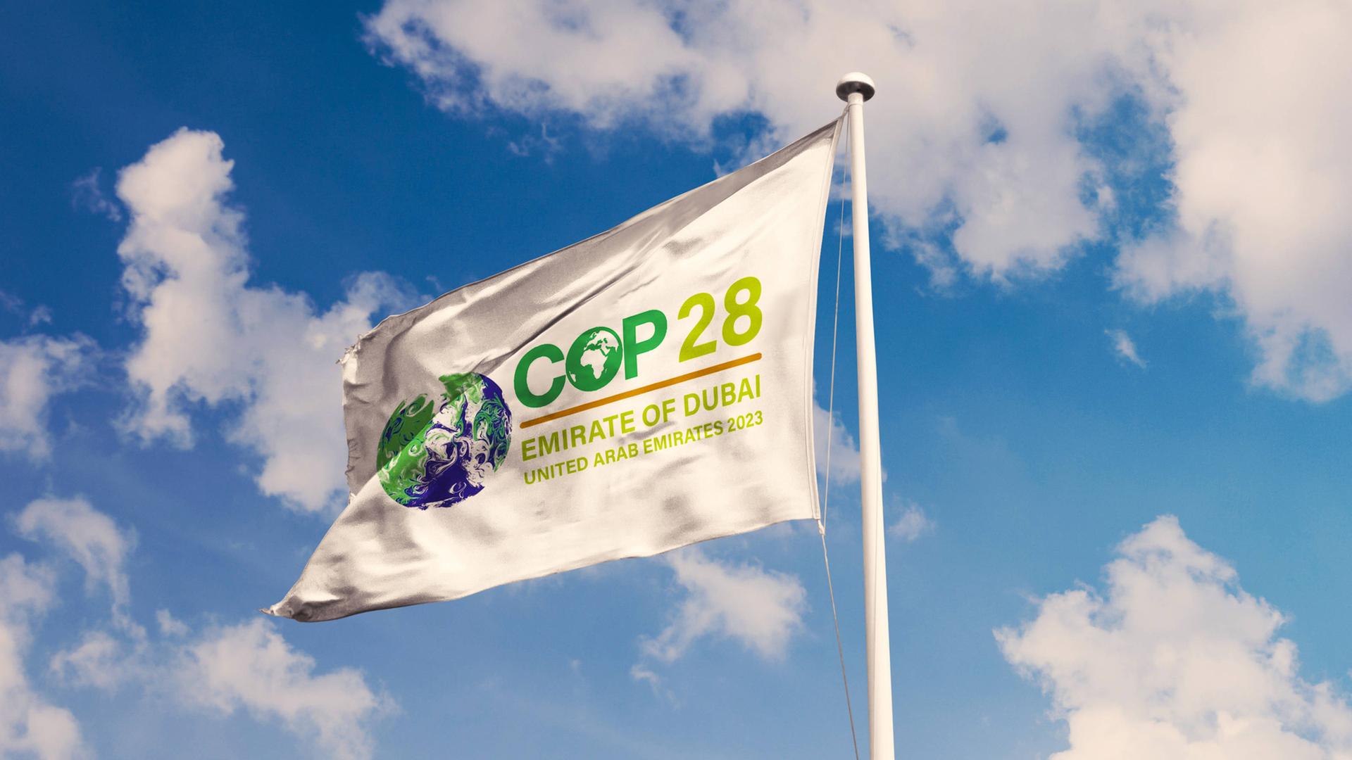Eine weiß Fahne mit dem Logo der Weltklimakonferenz COP28 flattert im Wind.