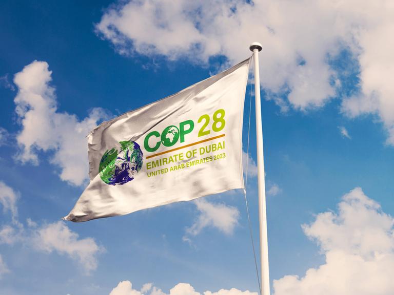 Eine weiß Fahne mit dem Logo der Weltklimakonferenz COP28 flattert im Wind.