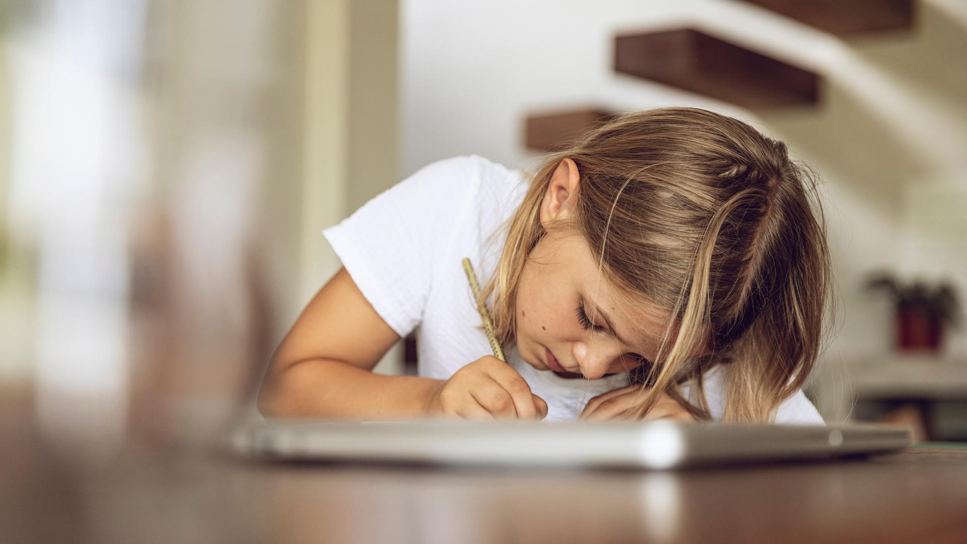 Ein Kind sitzt mit Stift und Notizbuch über einen Tisch gebeugt und schreibt. Ein Kind sitzt mit Stift und Notizbuch über einen Tisch gebeugt und schreibt.