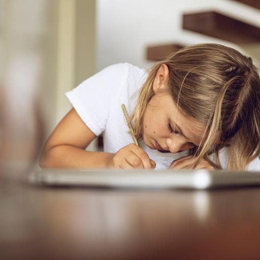 Ein Kind sitzt mit Stift und Notizbuch über einen Tisch gebeugt und schreibt.