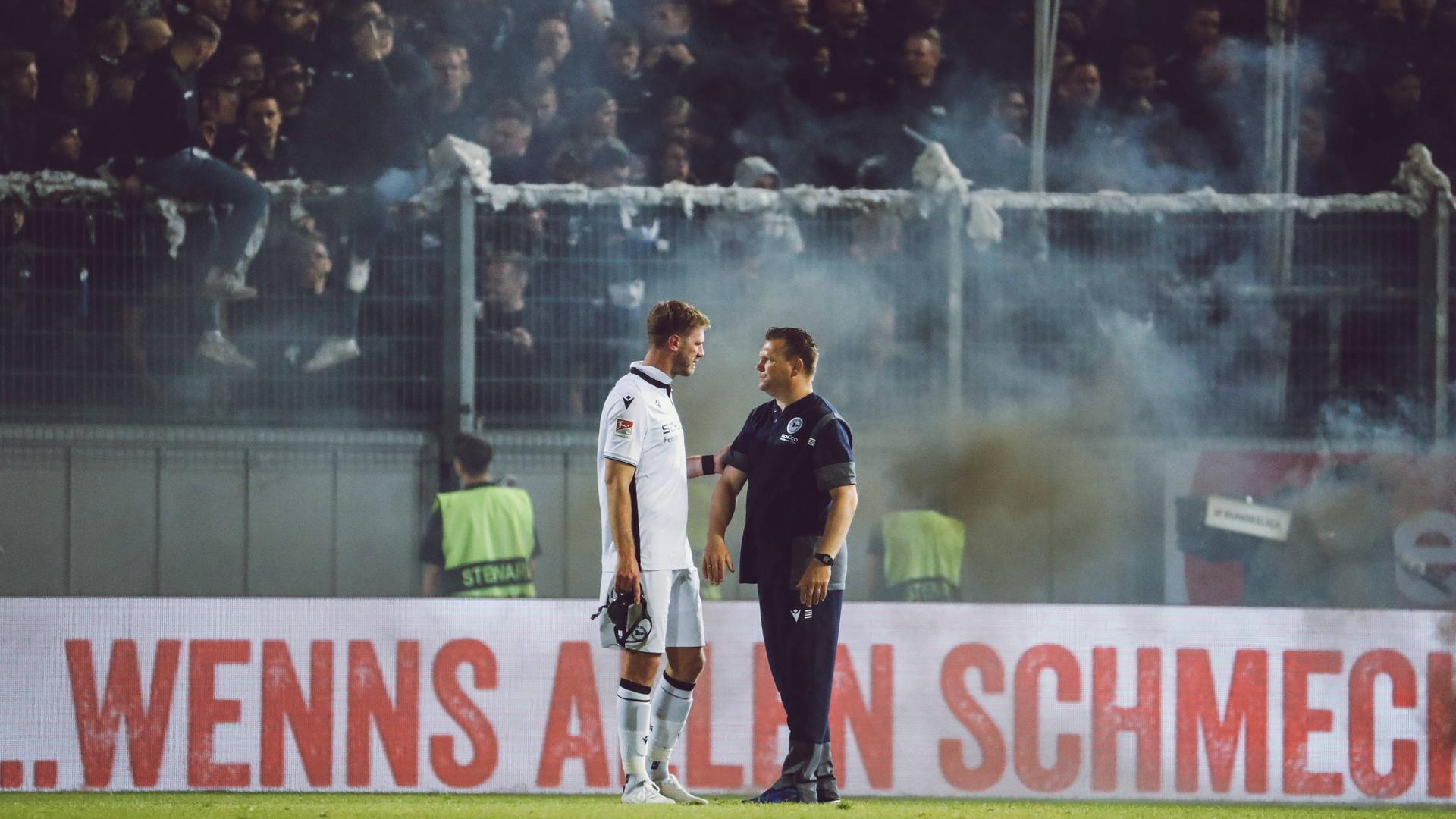 Die Fans von Arminia Bielefeld sorgten im Relegations-Hinspiel in Wiesbaden für eine knapp 20-minütige Spielunterbrechung. Kapitän Fabian Klos und Trainer Uwe Koschinat stehen vor der Fankurve.