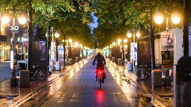 Eine Radfahrerin fährt am frühen Morgen zwischen Straßenlaternen durch die Innenstadt. 