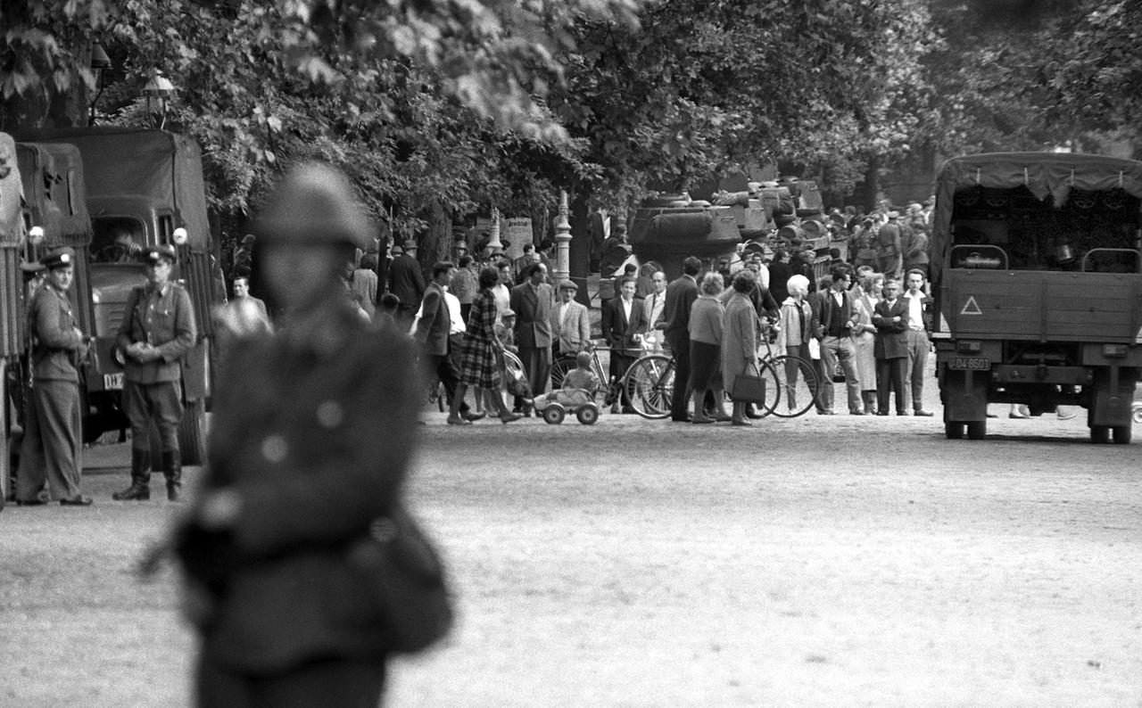Die Silhouette eines Volkspolizisten mit Gewehr im Anschlag, im Hintergrund verängstigt wartende Ostberliner, aufgenommen im August 1961 in der Swinemünder Straße im Wedding.