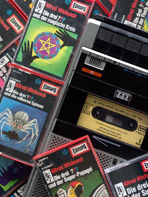Viele Hörspielkassetten der "Die drei Fragezeichen" liegen um einen Kassettenrekorder herum.