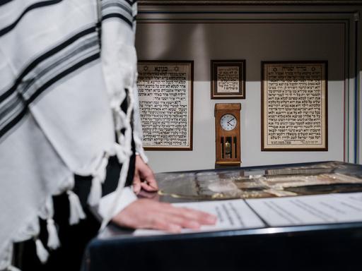 Eine Person mit einem über die Schultern geworfenen Tallit steht vor einer hebräischen Schrift.