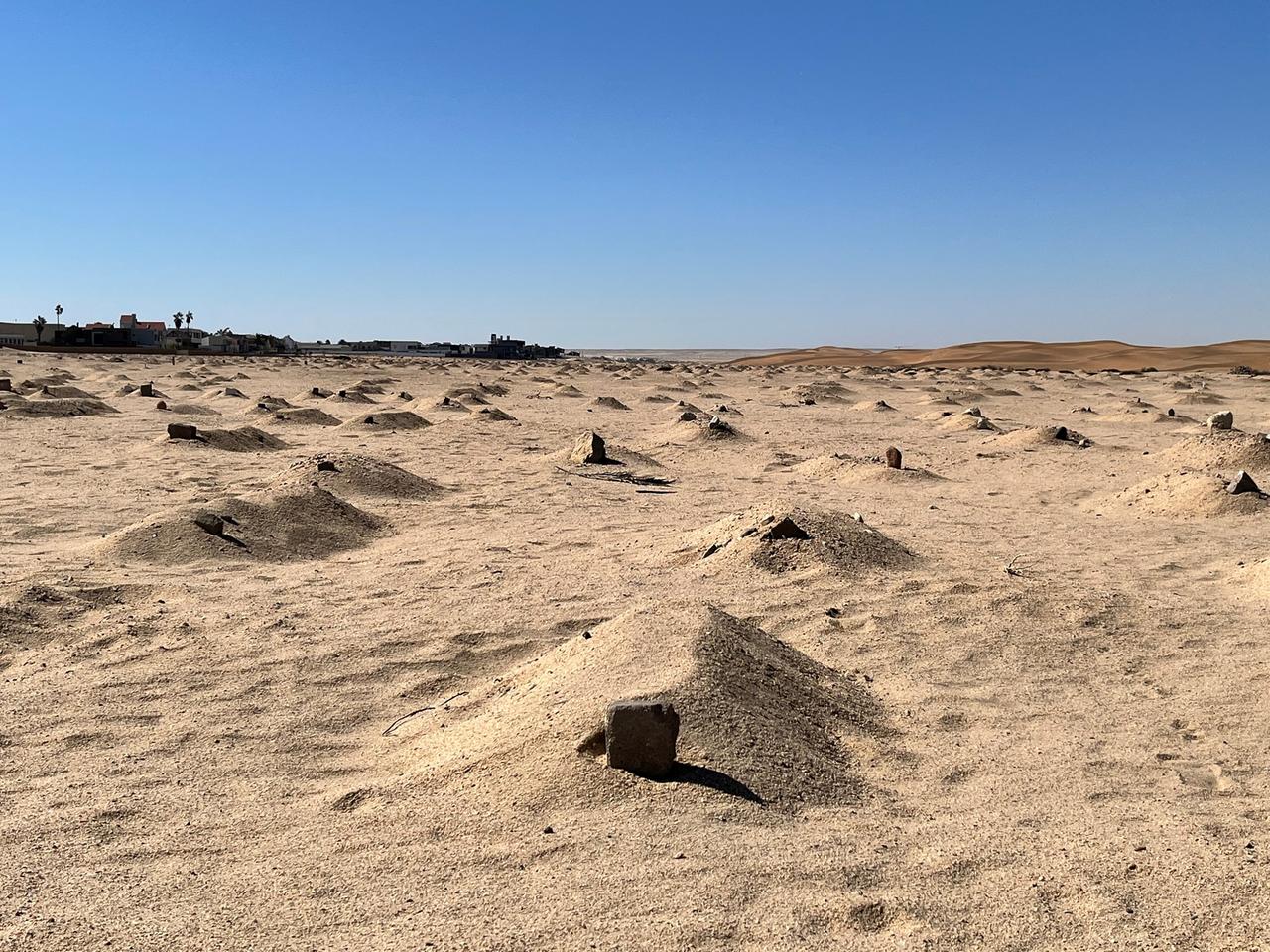 Sandhügel und Steine zwischen Wüste und Wohnsiedlung: Gräber von Herero auf dem Friedhof in Swakopmund.