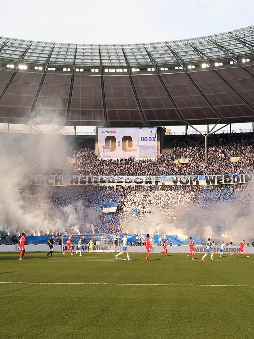 Spieler des Fußball-Derbys Hertha BSC Berlin gegen 1.FC Union Berlin vor Feuerwerk in der Ostkurve