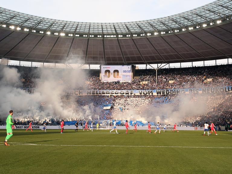 Spieler des Fußball-Derbys Hertha BSC Berlin gegen 1.FC Union Berlin vor Feuerwerk in der Ostkurve