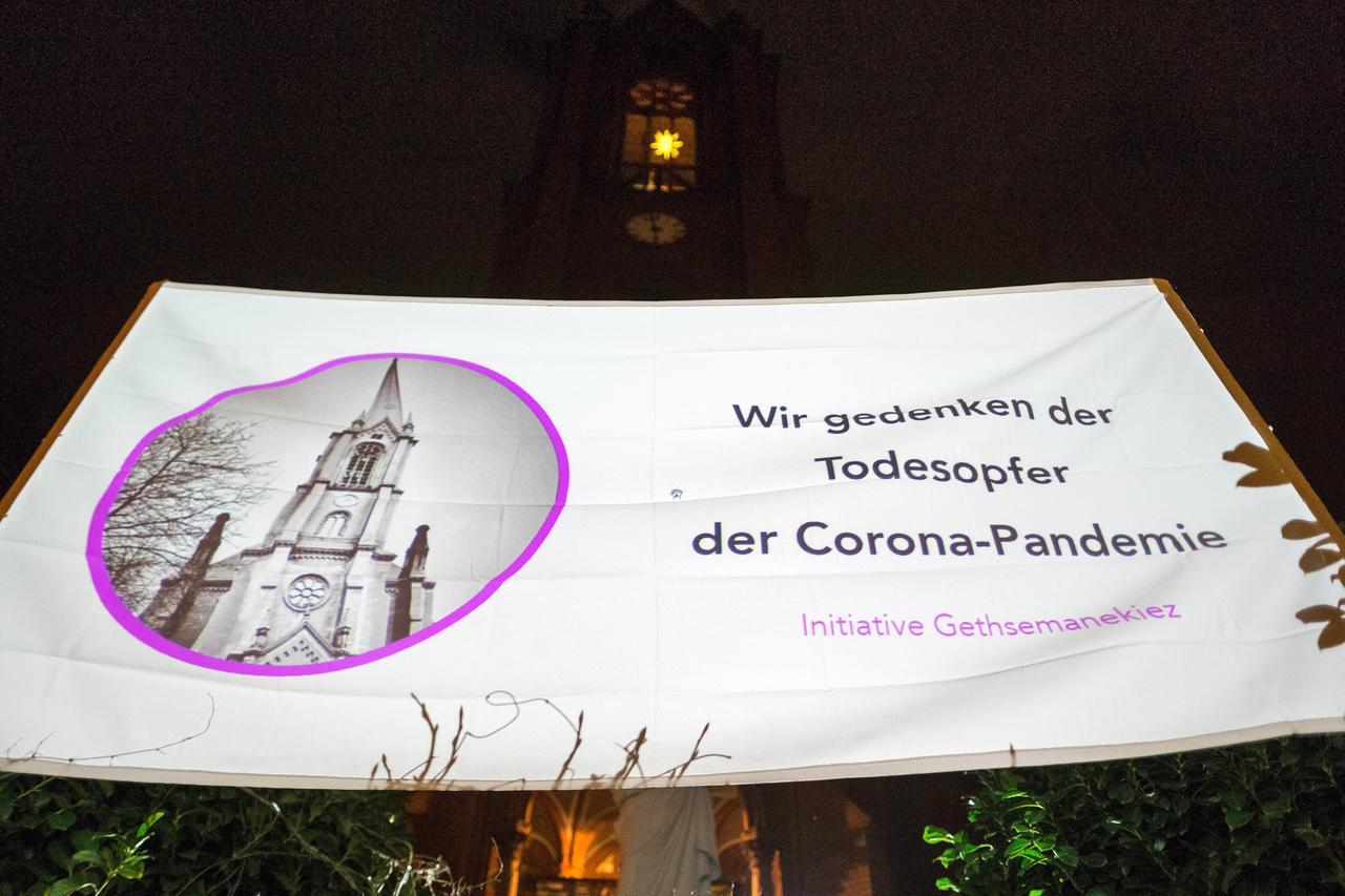 Ein weißes Stofftransparent mit der Aufschrift "Wir gedenken der Todespofer der Corona-Pandemie" und einer Fotografie der Gethsemanekriche.
