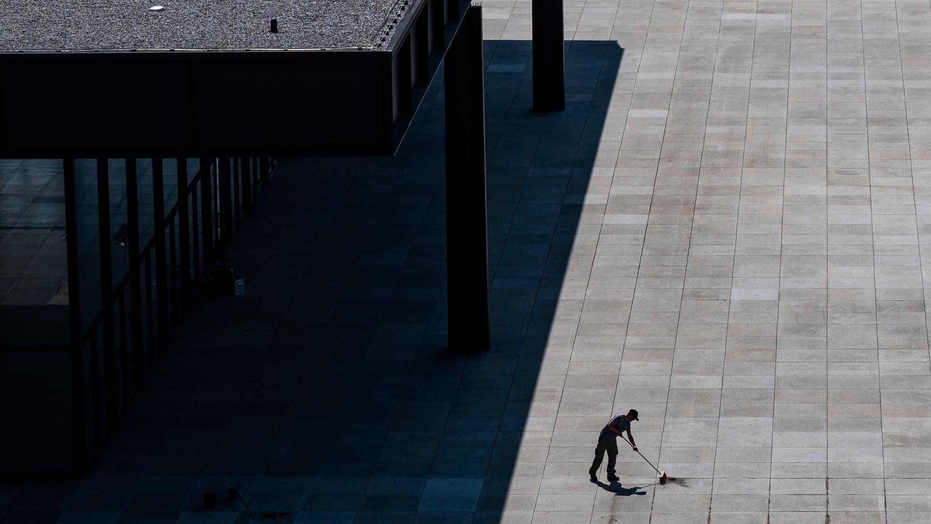 Ein Mann fegt den grauen Boden vor dem Gebäude der Neuen Nationalgalerie in Berlin.