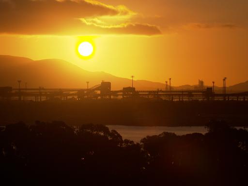 Ein prachtvoller Sonnenuntergang hinter den Bergen. Im Vordergrund im Dunkeln ein Hafen.