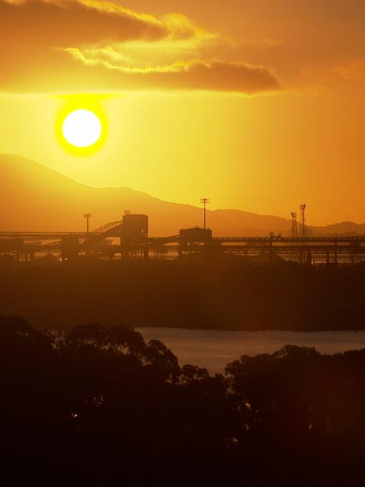 Ein prachtvoller Sonnenuntergang hinter den Bergen. Im Vordergrund im Dunkeln ein Hafen.