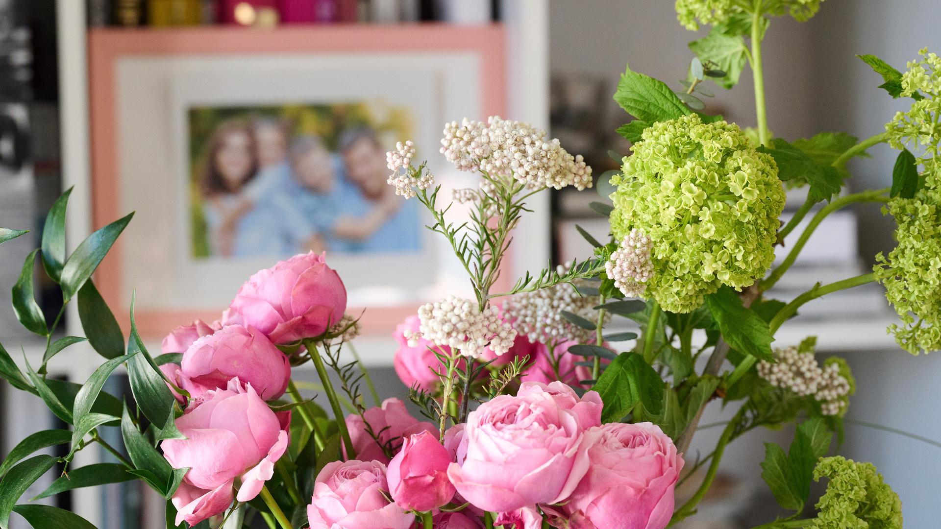 Ein Blumenstrauß steht in einem Wohnzimmer, während im Bücherregal ein Familienfoto steht.