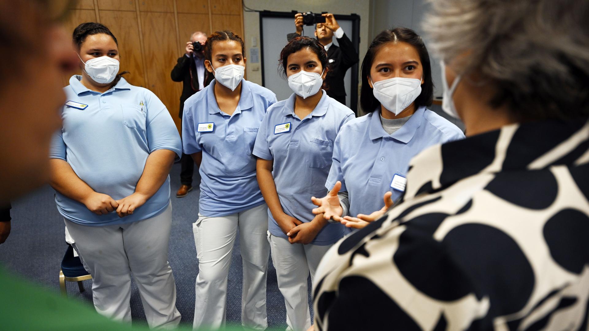 Vier weibliche Auszubildende aus El Salvador stehen Maske tragend nebeneinander und sprechen mit Thüringens Gesundheitsministerin. Vier weibliche Auszubildende aus El Salvador stehen Maske tragend nebeneinander und sprechen mit Thüringens Gesundheitsministerin.