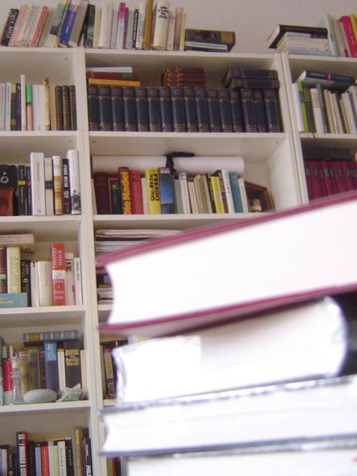 Ein Stapel Bücher vor einem Bücherregal.