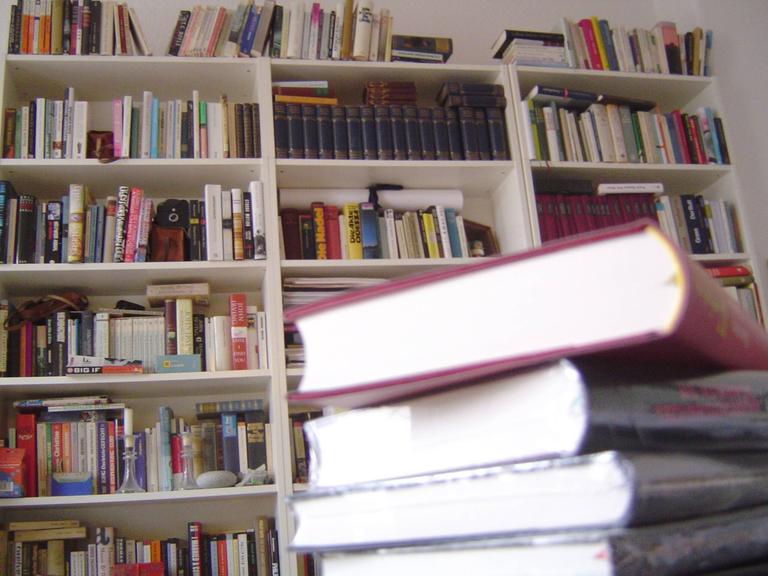 Ein Stapel Bücher vor einem Bücherregal.