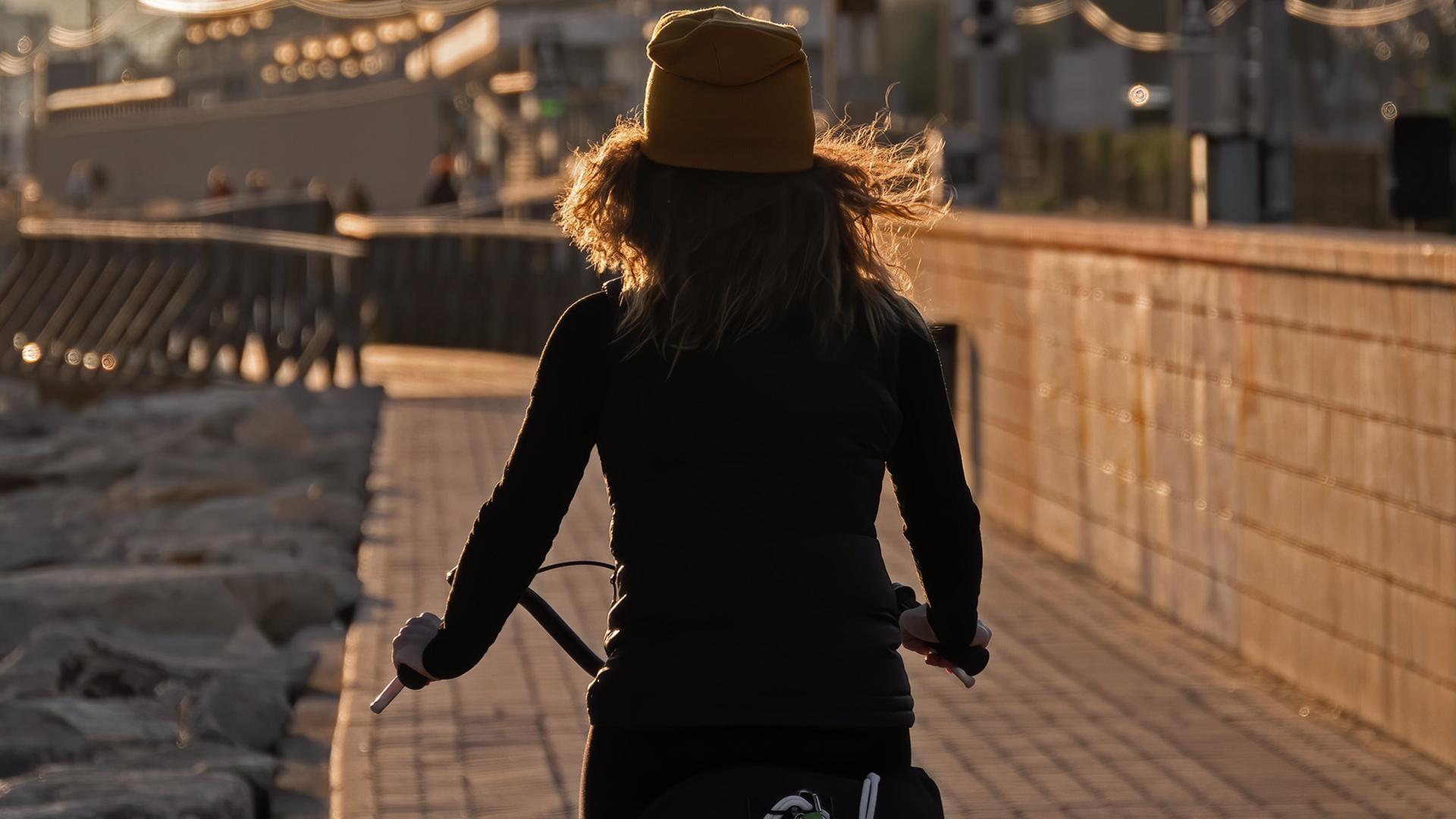 Eine junge Frau mit dem Rücken zur Kamera fährt auf einem Fahrrad.