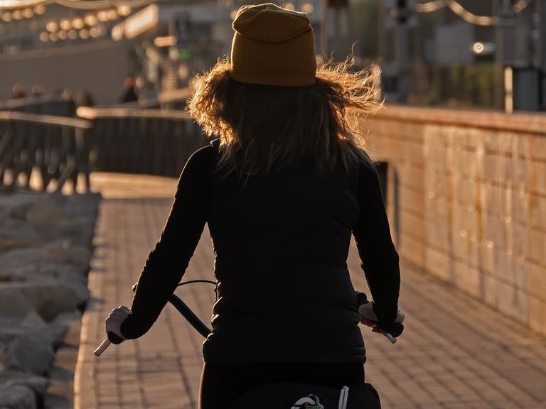 Eine junge Frau mit dem Rücken zur Kamera fährt auf einem Fahrrad.
