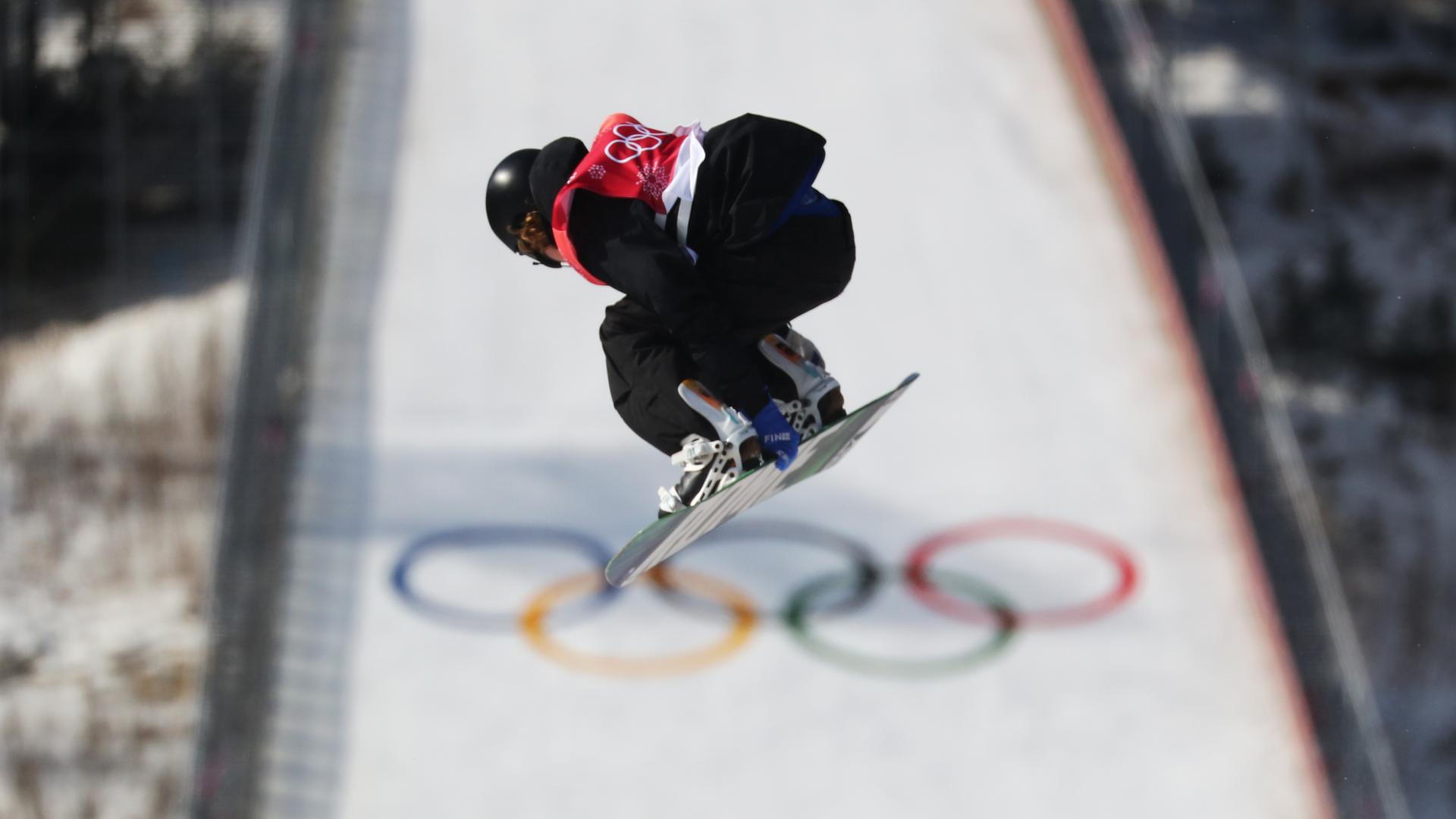 Petr Horak in gebeugter Haltung in der Luft auf seinem Snowboard. Im Hintergrund eine Schanze mit den Olympischen Ringen.