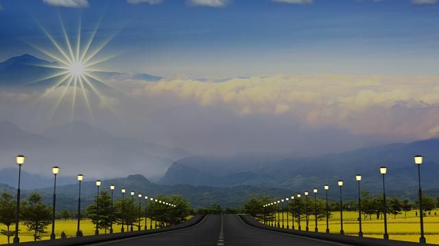 Bäume und Straßenlaternen rechts und links entlang einer Straße, die durch eine Hügellandschaft führt, oben links die Sonne.