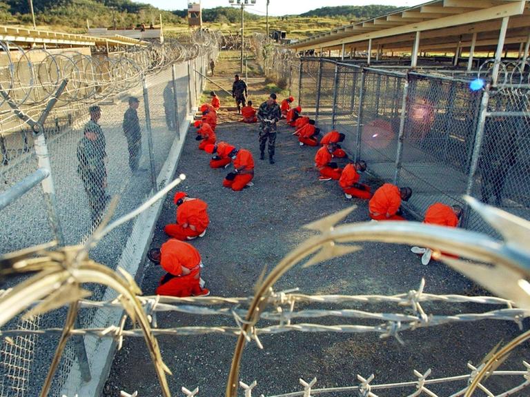 In orangefarbene Overalls gekleidet sitzen Häftlinge in einem mit Stachelraht abgesperrten und von US-Wärtern bewachten Bereich des Gefängnisses in Guantanamo auf der Insel Kuba. 