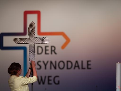 Eine Frau steckt während der vierten Synodalversammlung der katholischen Kirche in Deutschland im Congress Center Messe Frankfurt dem Synodalkreuz ein rotes kleines Kreuz an.