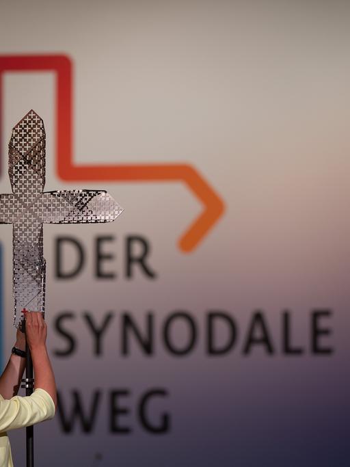 Eine Frau steckt während der vierten Synodalversammlung der katholischen Kirche in Deutschland im Congress Center Messe Frankfurt dem Synodalkreuz ein rotes kleines Kreuz an.